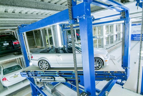 Silver car in a blue metal frame being lowered into a parking facility.